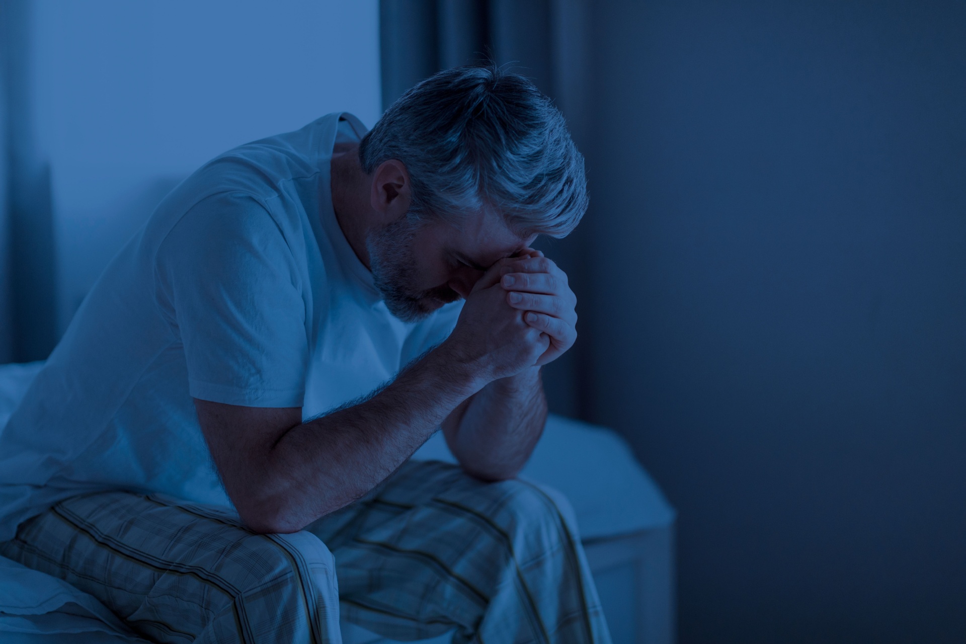 Mann som sitter på sengekanten midt på natten, får ikke sove