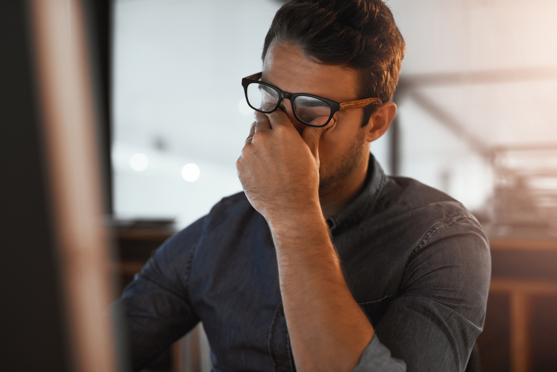 Ung mann gnir seg i øynene under brillene sine, stresset med jobb